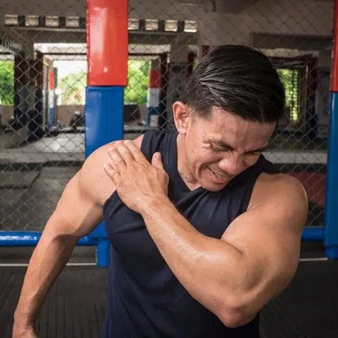 A fit man experiences rotator cuff tear sprain or injury during a workout session at the gym.